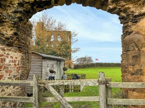 A rustic stone archway leading to a wooden cabin with a small garden and a flag. - The Shepherds Hut - UK50986 (Sheriff Hutton)