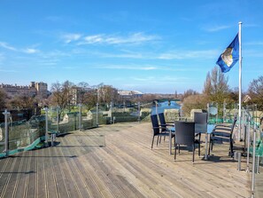 A wooden deck with chairs and a flag, overlooking a river and buildings. - 3 bedroom accommodation in York (York)