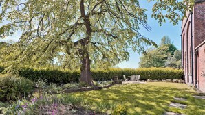 Un giardino con un albero, un siepe e un edificio in mattoni.