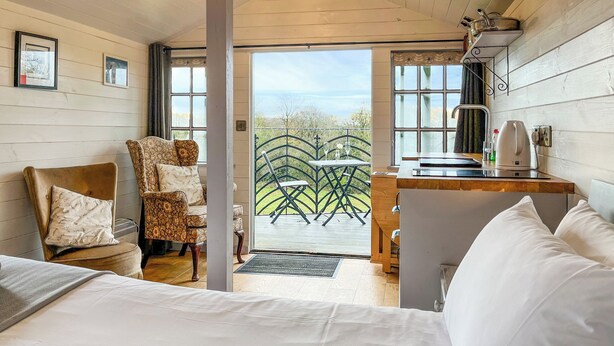 Um quarto acolhedor com uma cama, uma cadeira, uma pequena mesa com chaleira e vista para o exterior.