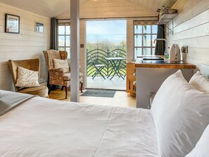 Um quarto acolhedor com uma cama, uma cadeira, uma pequena mesa com chaleira e vista para o exterior.