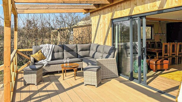Un espace extérieur aménagé, abrité, avec un canapé d’angle, des fauteuils en osier et une petite table.