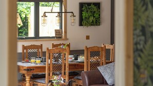 Un coin repas avec des chaises en bois, une table où sont disposés des aliments pour le petit-déjeuner et un luminaire suspendu.