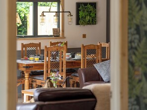 A dining area with wooden chairs, a table with breakfast items, and a hanging light fixture. - Fern Lodge - UK36772 (Chichester)