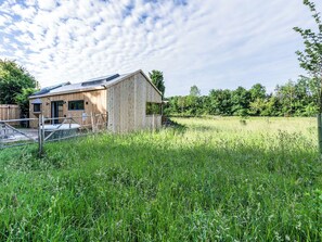 Eine Holzhütte mit geneigtem Dach, einem umzäunten Hof und einer natürlichen Landschaft mit Bäumen und Gras.