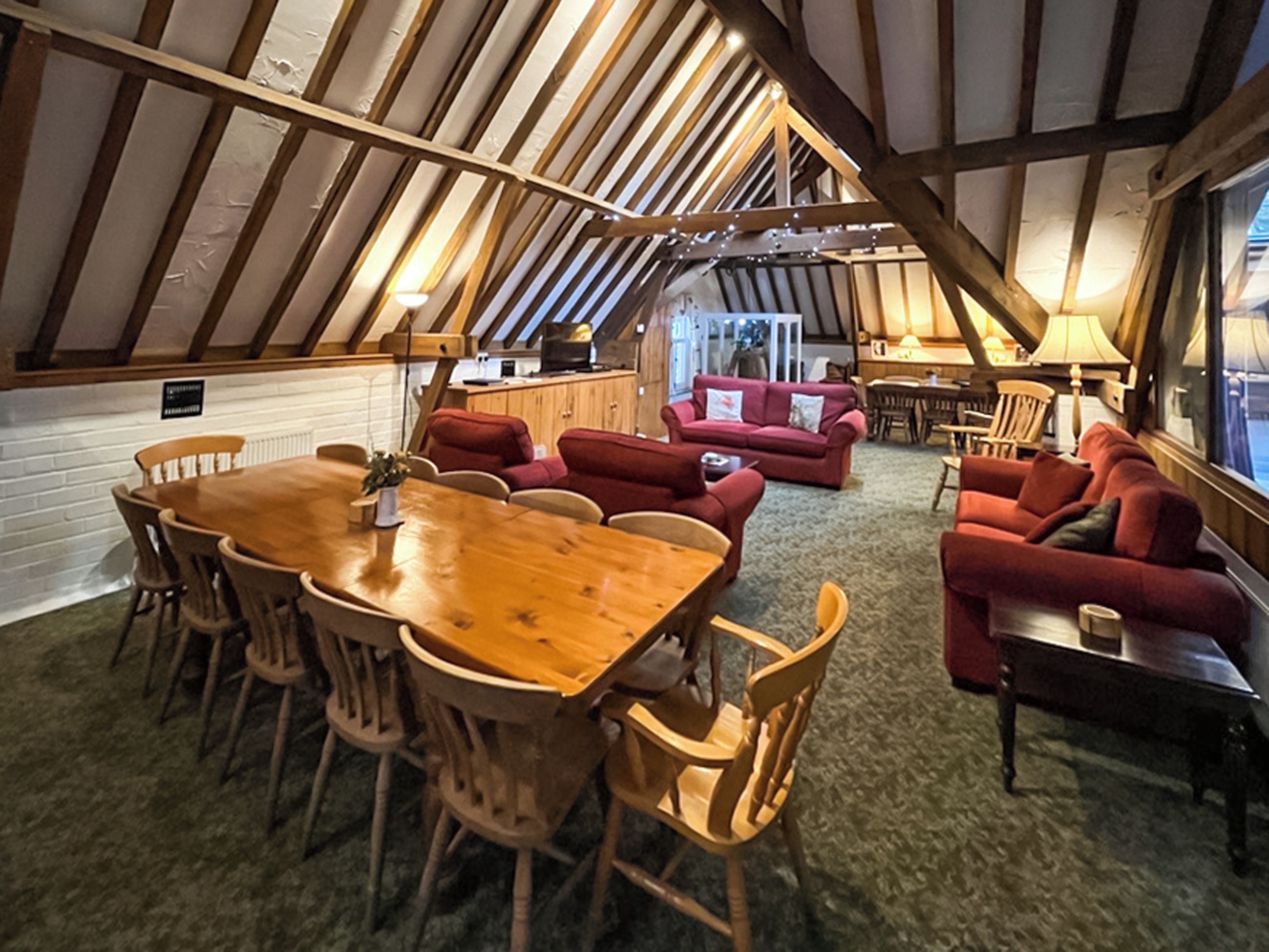 Ein gemütliches Dachzimmer mit Holztisch, roten Sofas und einer Küchenzeile.