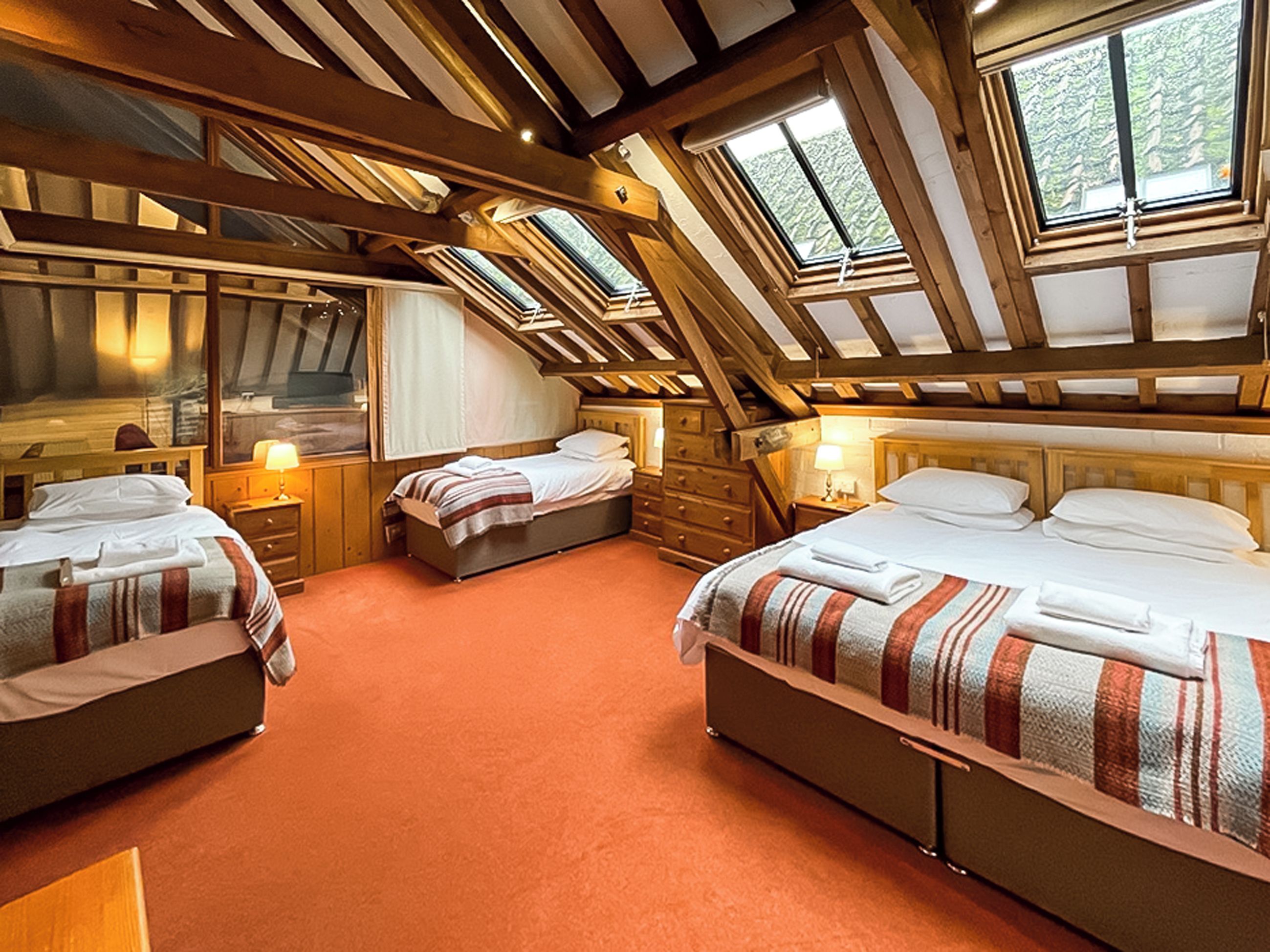 A room with three beds, wooden beams, and skylights.