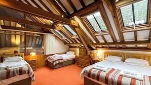 Une chambre avec trois lits, des poutres en bois et des fenêtres de toit.