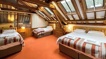 A room with three beds, wooden beams, and skylights.