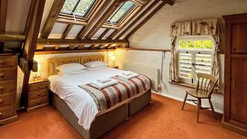 A bedroom with a sloped ceiling, a bed with white linens, a wooden chair, and a window with curtains.