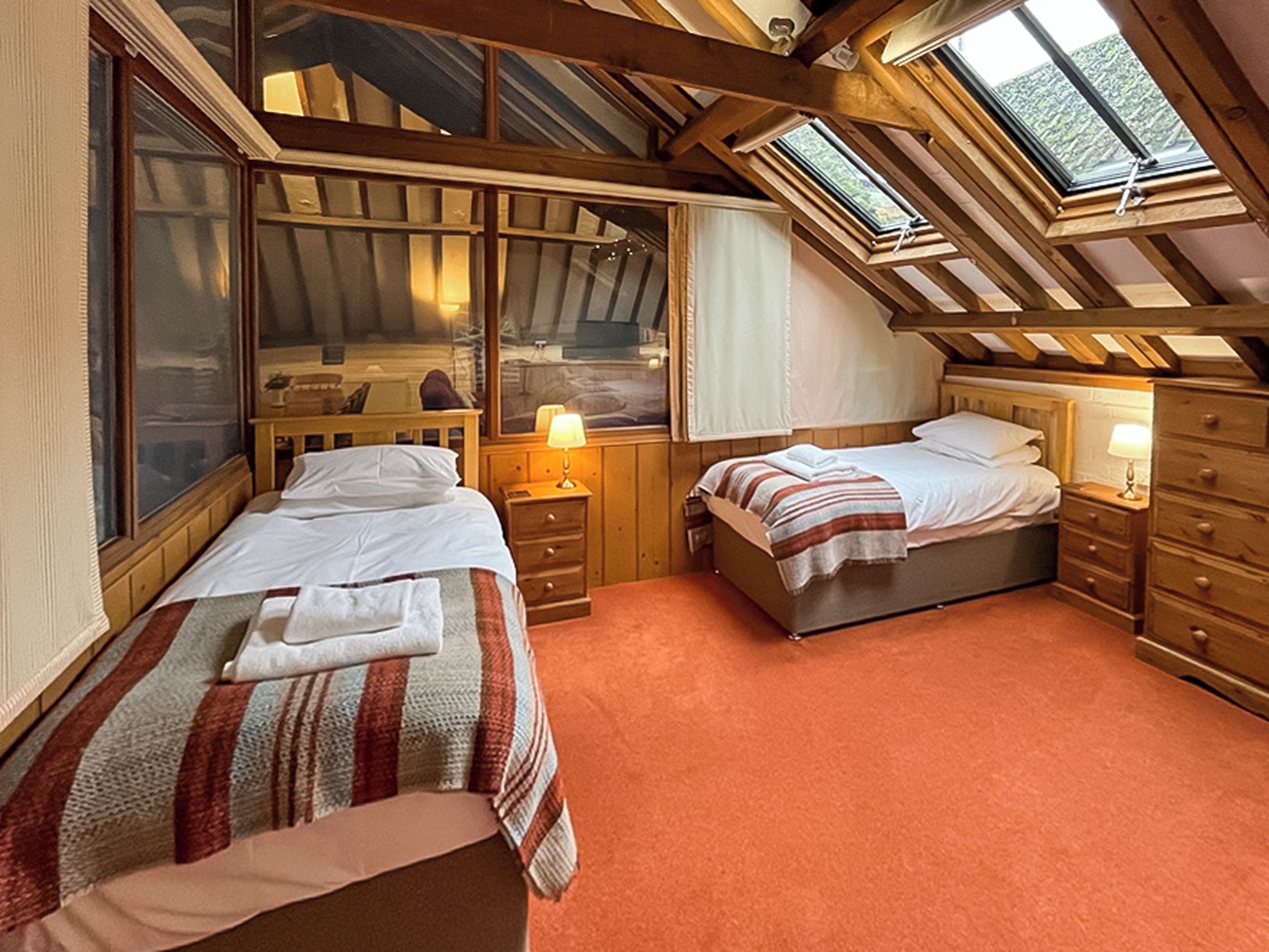 A bedroom with two beds, wooden headboards, a skylight, and a window.