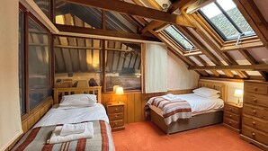 Une chambre avec deux lits, des têtes de lit en bois, une lucarne et une fenêtre.