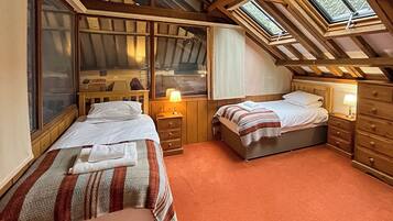 A bedroom with two beds, wooden headboards, a skylight, and a window.