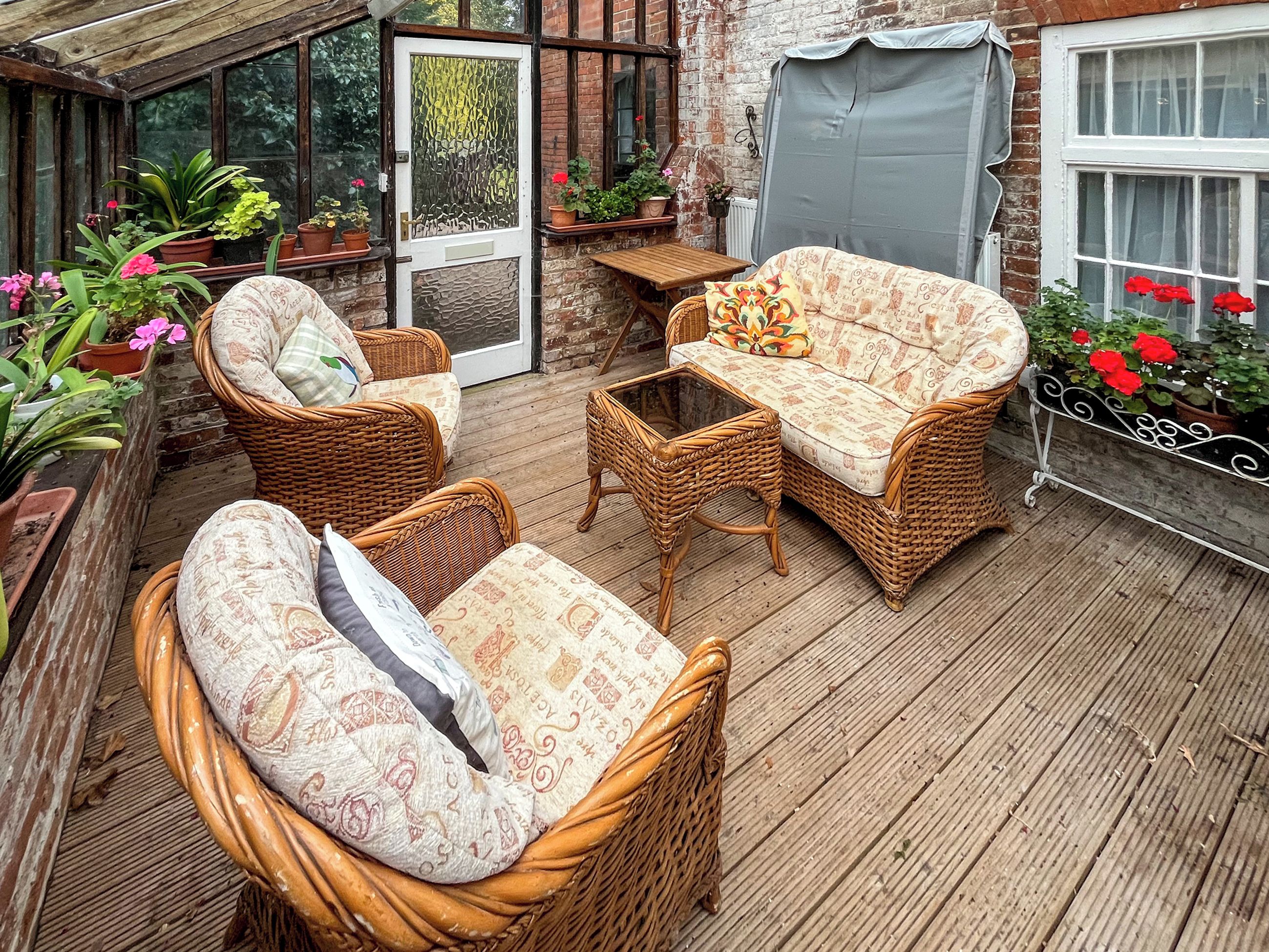 A covered patio with wicker furniture, potted plants, and a view of the garden.