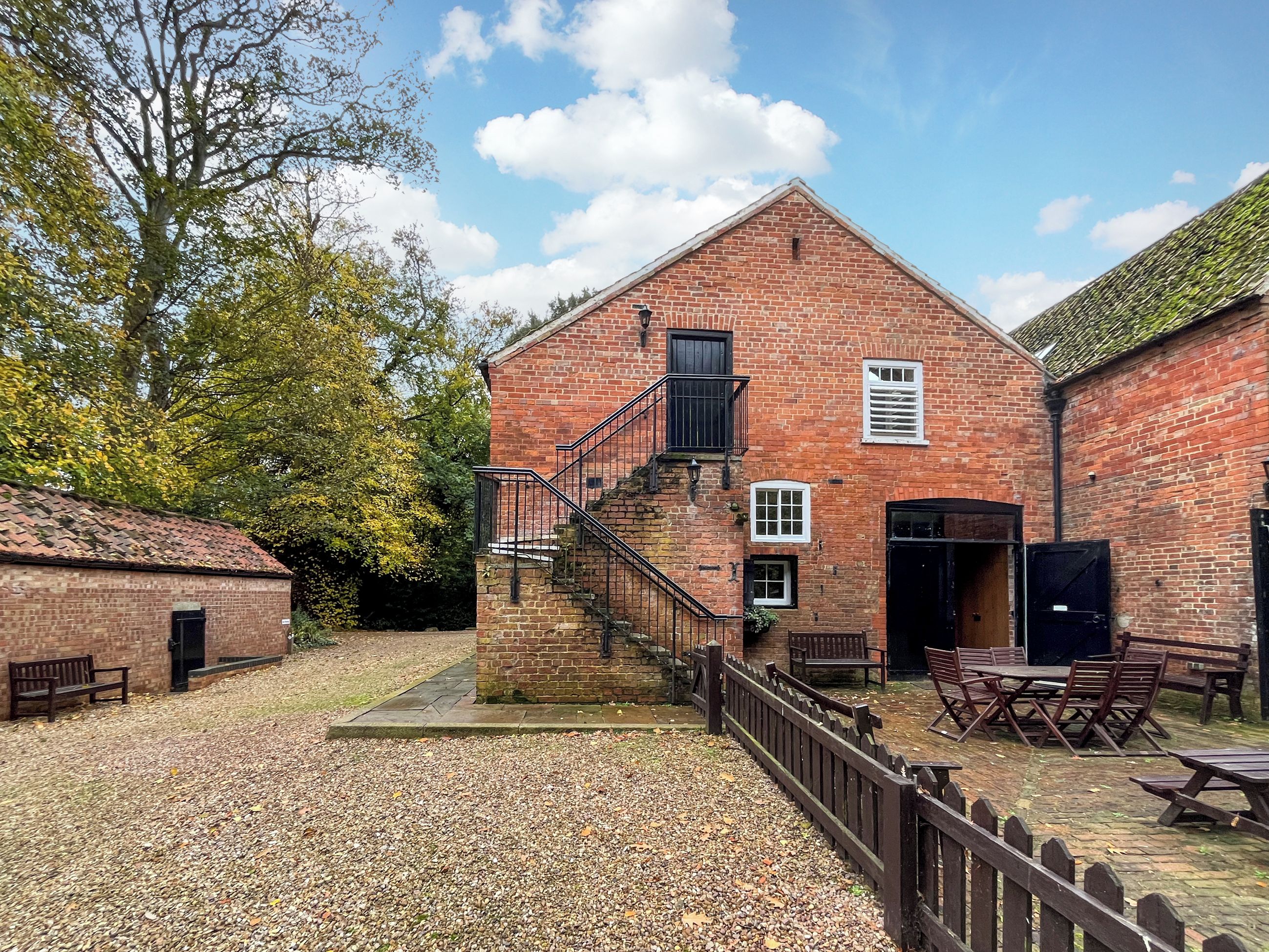 A brick building with a staircase leading to a second floor. There are outdoor seating areas with tables and benches.