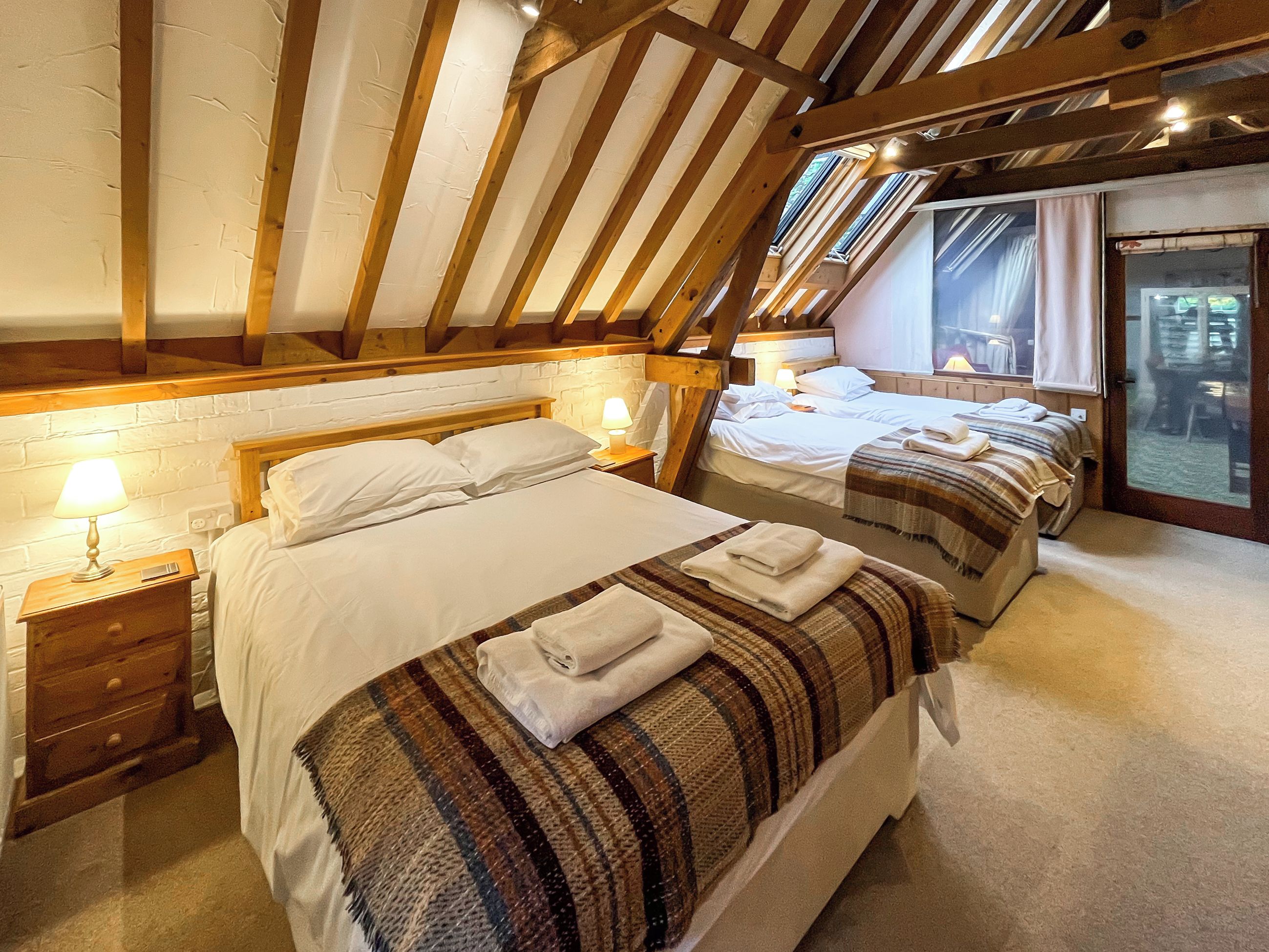 A bedroom with two beds, wooden beams, a brick wall, and a window.