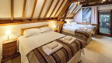A bedroom with two beds, wooden beams, a brick wall, and a window.
