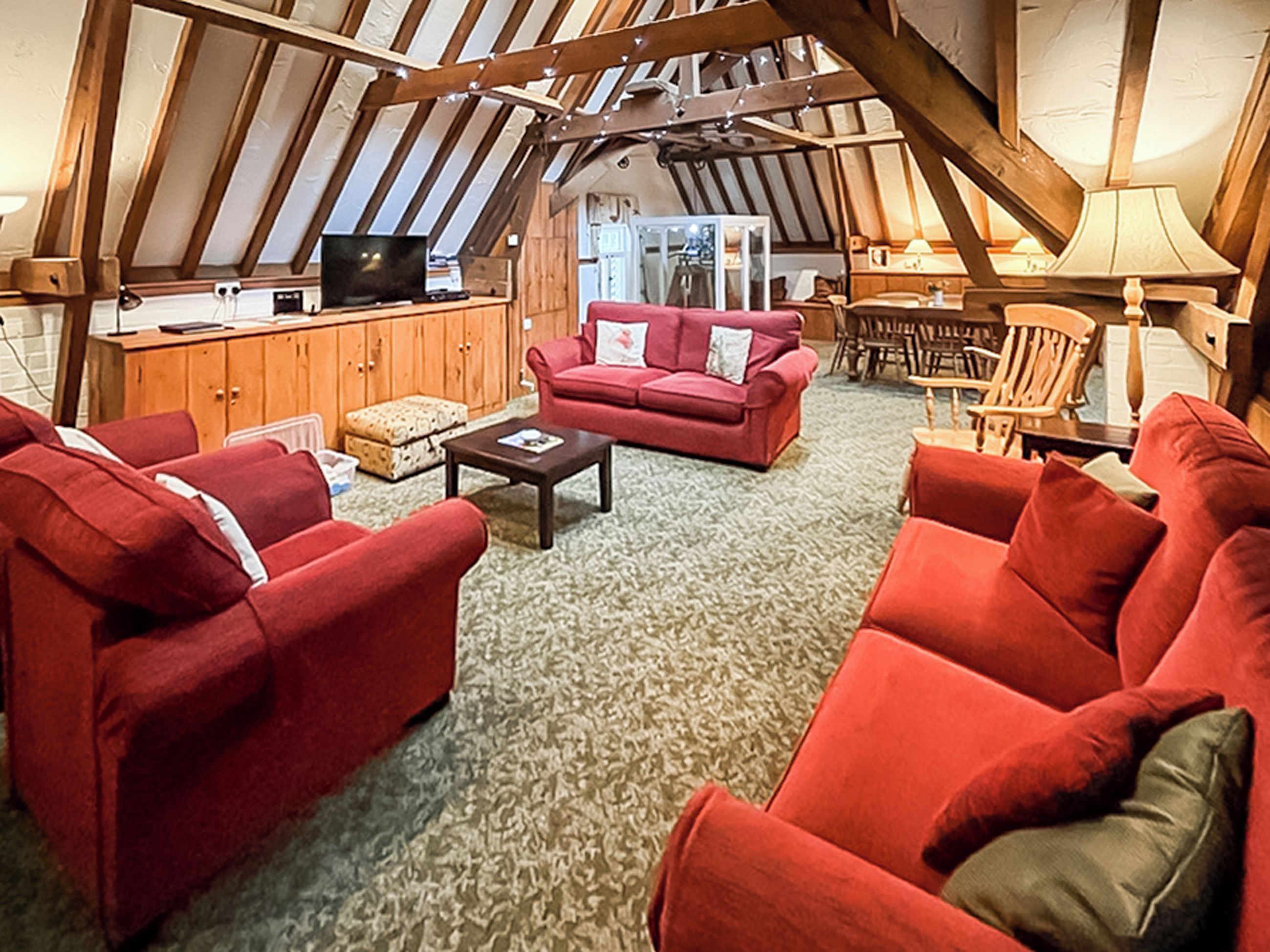 Een gezellige woonkamer met rode banken, een bijzettafeltje en een houten plafond.