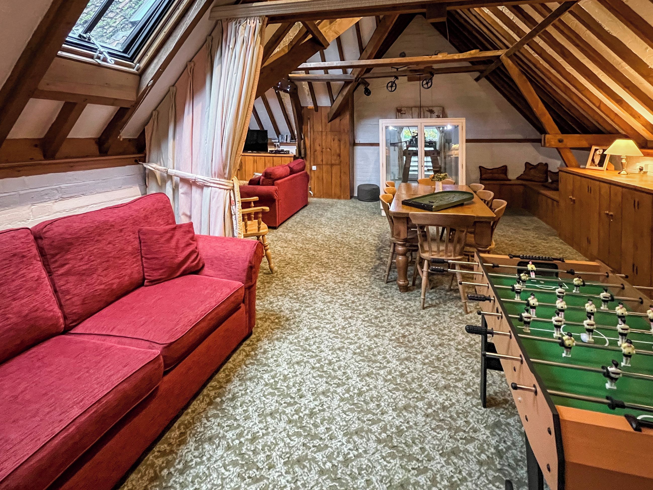 A cozy attic room with a red sofa, a foosball table, and a dining area.
