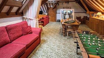 A cozy attic room with a red sofa, a foosball table, and a dining area.