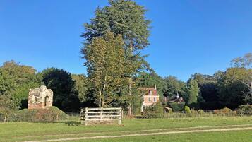 A rural landscape with a stone ruin, a tall tree, and a red house.