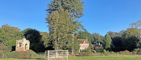 A rural landscape with a stone ruin, a tall tree, and a red house.