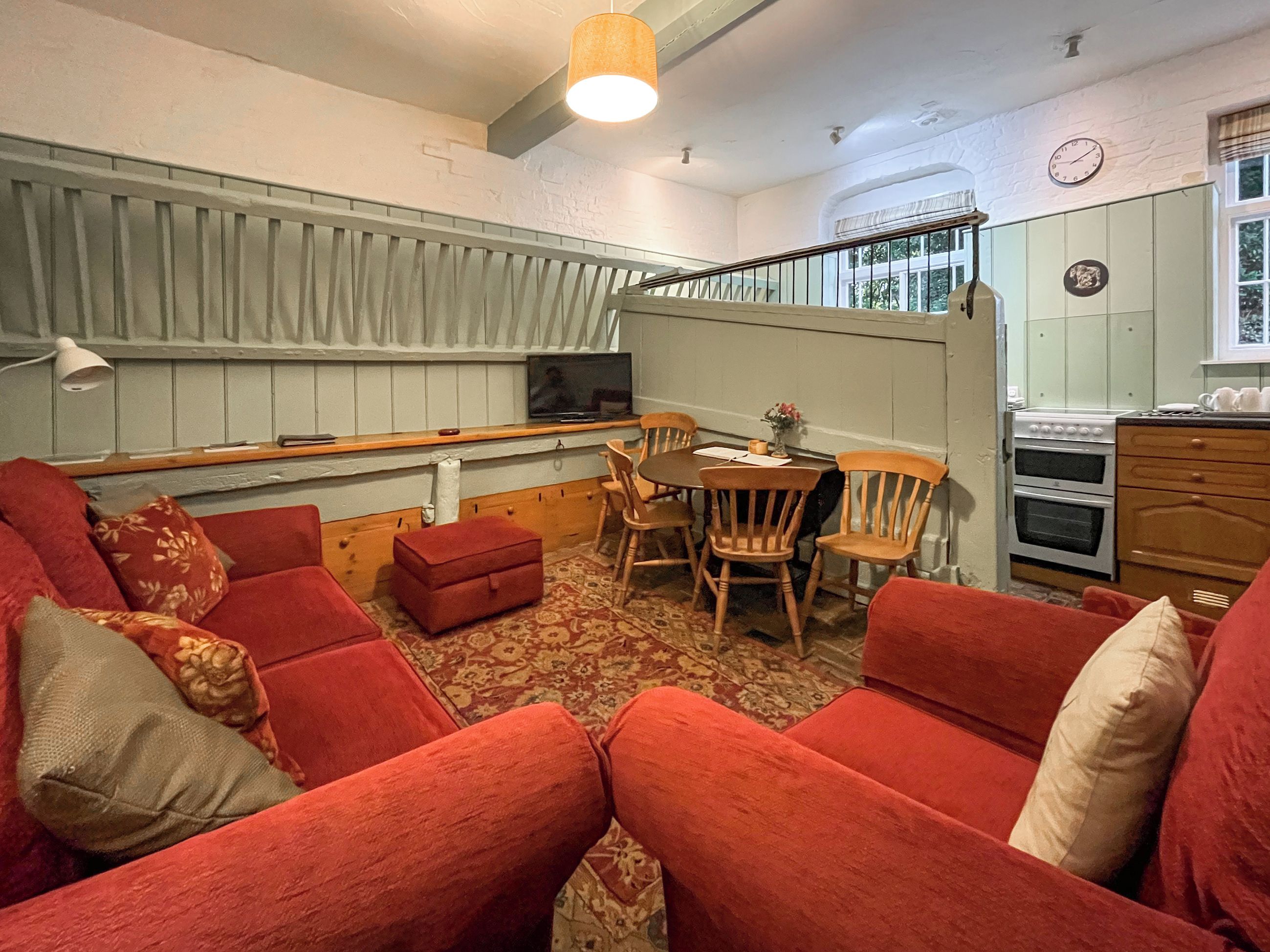 A cozy living room with red sofas, a wooden dining table, and a kitchen area with a stove and cabinets.