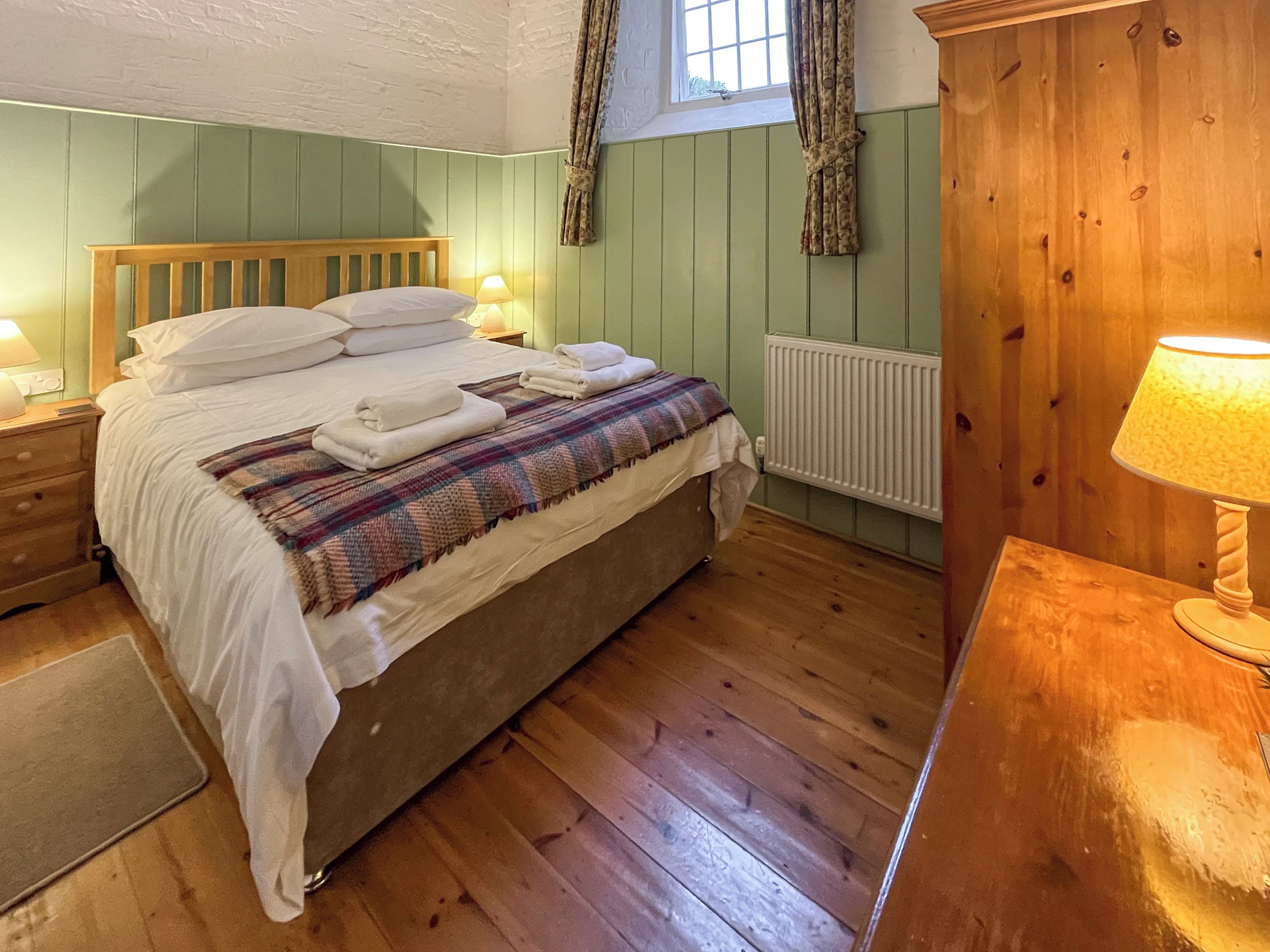 Ein gemütliches Schlafzimmer mit einem hölzernen Bett, einer Karo-Decke und einem Nachttisch mit einer Lampe.