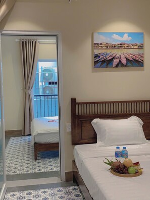 A hotel room with a bed, a window with curtains, a painting of boats, and a fruit basket on the bed.