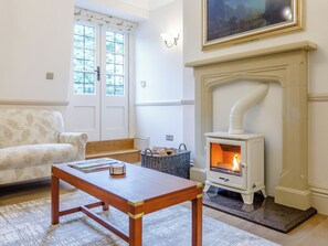 A living room with a sofa, a table, a fireplace, and a window with curtains. - Eagles Nest at Greyfriars - UK33356 (Winchelsea)