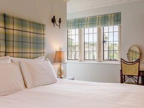 A bedroom with a bed, a lamp, a chair with a mirror, and a window with a view of a building. - Eagles Nest at Greyfriars - UK33356 (Winchelsea)