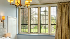 A bedroom with a large window, a chandelier, a bed, and a nightstand. - Heron's Wood at Greyfriars - UK33357 (Winchelsea)