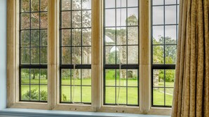 A window with multiple panes, a curtain on the right, and a view of a garden and stone structure outside. - Heron's Wood at Greyfriars - UK33357 (Winchelsea)