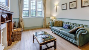 A room with a green sofa, a glass coffee table, a fireplace, and a large window with curtains. - Heron's Wood at Greyfriars - UK33357 (Winchelsea)