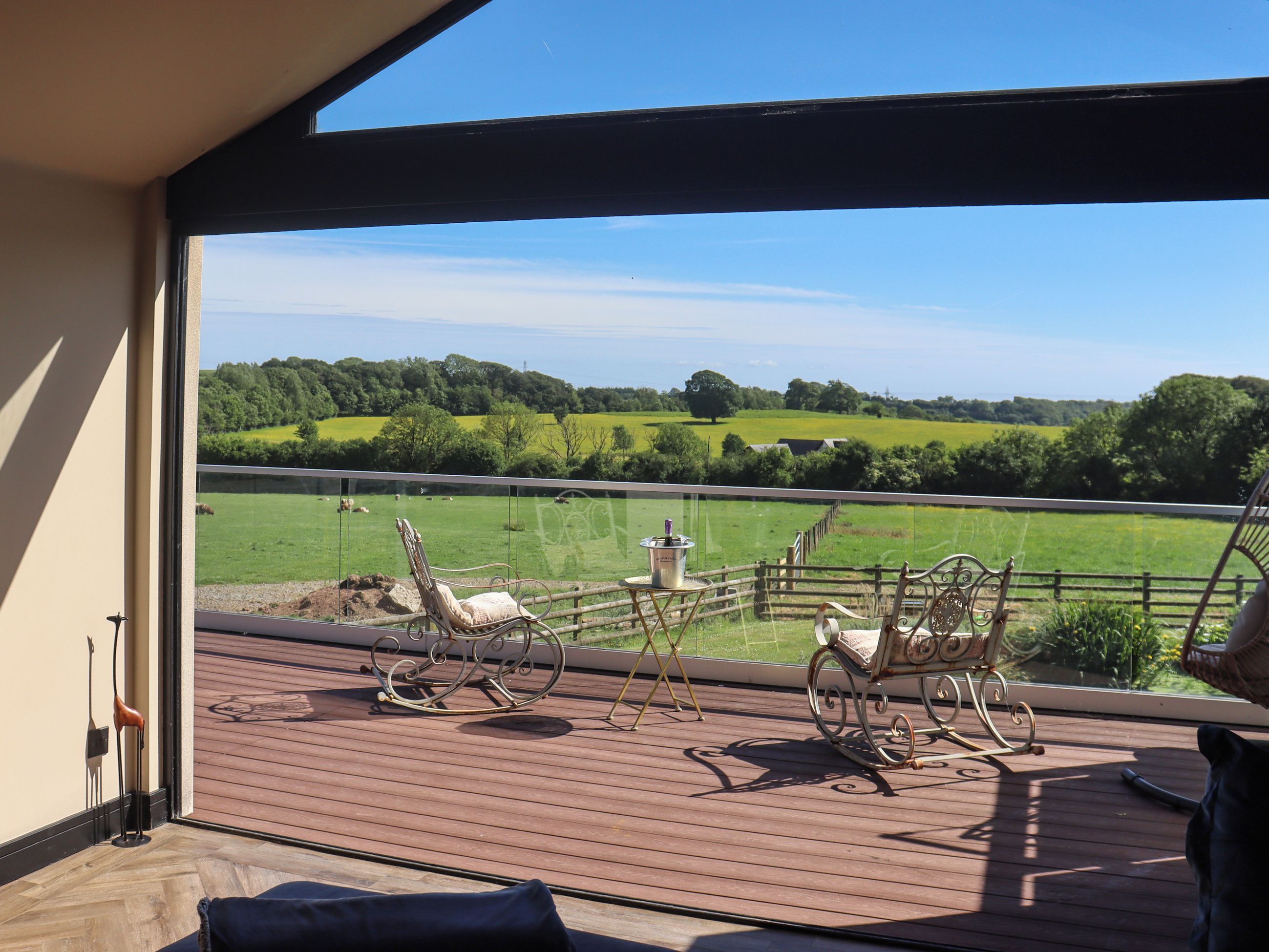 A balcony with a view of a green field and trees, furnished with metal rocking chairs and a small table.