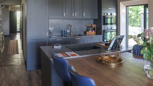 Een moderne keuken met grijze kastjes, roestvrijstalen apparatuur en een houten eettafel met blauwe stoelen.