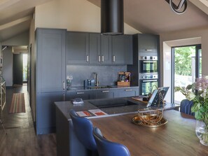 A modern kitchen with grey cabinets, stainless steel appliances, and a wooden dining table with blue chairs. - Deerview Stables - UK51043 (Bonvilston)