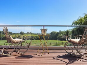 Un balcon agrémenté de deux fauteuils à bascule décoratifs et d’une petite table sur laquelle est posé un objet décoratif.