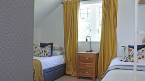 A bedroom with two beds, a bedside table, a window with curtains, and a patterned wall. - Deerview Lodge - UK51044 (Bonvilston)