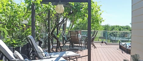 A deck with lounge chairs, a table, and a pergola with hanging lights.
