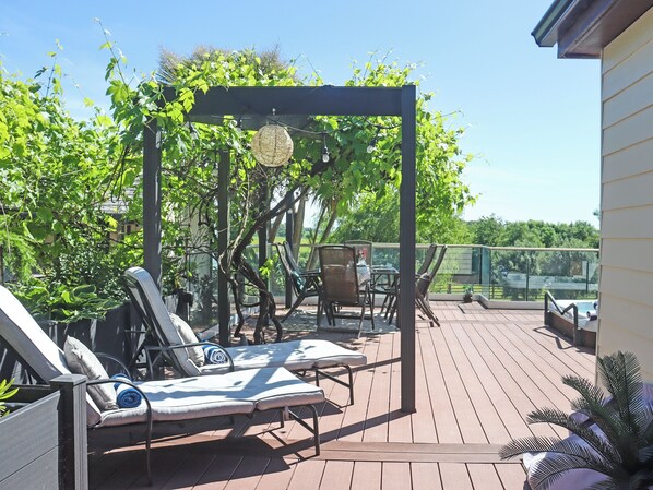 A deck with lounge chairs, a table, and a pergola with hanging lights.