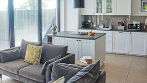 A modern kitchen with white cabinets, a black overhead light, and a dining area with a grey sofa. - Deerview Lodge - UK51044 (Bonvilston)