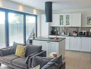 A modern kitchen with white cabinets, a black overhead light, and a dining area with a grey sofa. - Deerview Lodge - UK51044 (Bonvilston)