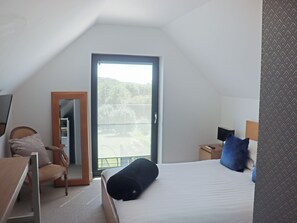 Ein Hotelzimmer mit einem Bett, einem Sessel, einem Schreibtisch, einem Spiegel und einer Tür, die auf einen Balkon führt.