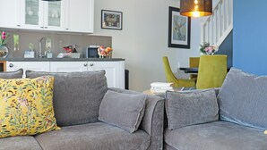 A grey sofa with a floral pillow, a kitchen with white cabinets, and a dining area with a yellow chair. - Deerview Lodge - UK51044 (Bonvilston)