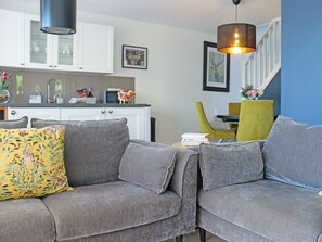 A grey sofa with a floral pillow, a kitchen with white cabinets, and a dining area with a yellow chair. - Deerview Lodge - UK51044 (Bonvilston)