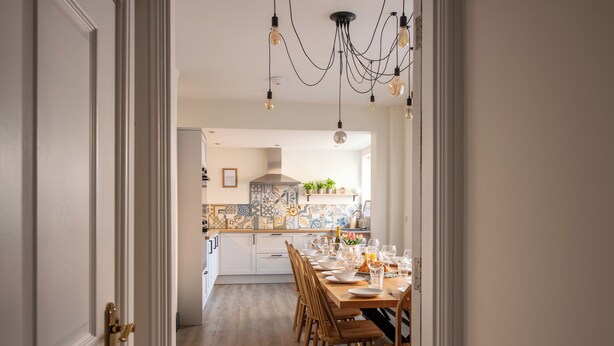 A modern kitchen with a dining area, featuring a long wooden table, chairs, and a variety of kitchen appliances.