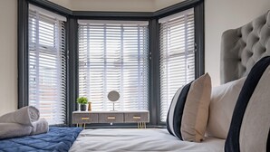 A bedroom with a bed, a bedside table with a mirror, and a window with blinds.