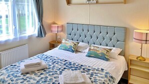 Un letto rifatto con cura, una coperta a fiori, due lampade sui comodini, una testiera e una mensola con un cartello con la scritta 'LOVE'.