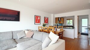 Una sala moderna con un sofá seccional gris, un comedor con sillas de madera y una cocina con armarios de madera.